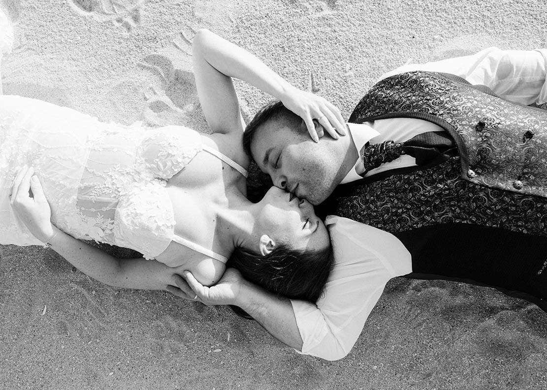 Bodas en primavera Galicia, fotografía Sanoguera Pareja de novios besándose tumbados en la arena durante su boda en Galicia